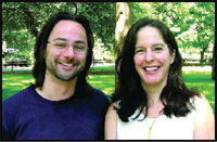 A man with glasses and a woman with long dark hair smiling together in a park.