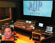 A large audio mixing console in a dark studio with a bright screen displaying 'POP SOUND' in the background.