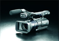A black professional video camcorder with a large lens and microphone on a dark, reflective surface.