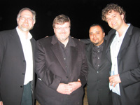 Four men in suits and dress shirts posing together against a dark background.