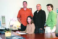 Four people, one woman seated and three men standing, pose in an office.