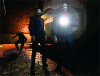 Two people stand in a dark alley, one holding a bright light source that creates a lens flare.