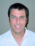 A smiling man with short dark hair and light eyes wearing a light blue button-down shirt.