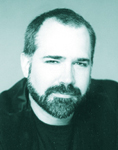 A headshot of a man with short hair and a dark beard against a light background.