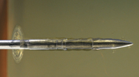 A macro view of a sharp, metallic needle tip pointing to the right against a blurred background.