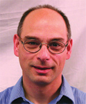 A man with short hair and glasses wearing a blue button-down shirt.