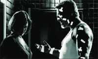 Black and white profile of a man in a tank top gesturing toward a woman in shadow.