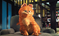An orange tabby cat with green eyes sits upright in a gray armchair in a dimly lit room.