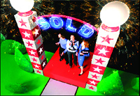 Three people stand on a red carpet under a blue neon 'SOLD' sign between two lit pillars with pink stars.