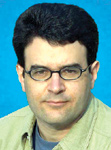 A man with dark hair and glasses wearing a light green shirt against a blue background.
