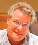 A man with curly hair and glasses smiling at the camera.