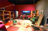 A messy room with red walls, wooden shelves, a small table, chairs, and scattered debris on the floor.