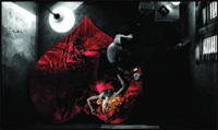 A person in white leans over a person lying on a large, red, teardrop-shaped fabric in a dark, shadowy room.
