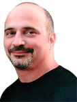A man with a shaved head and a dark goatee smiling slightly against a white background.