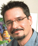A man with short dark hair, glasses, and a goatee smiling against a light background.
