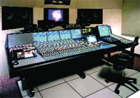 A large professional audio mixing console with numerous sliders and knobs in a recording studio.