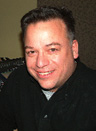 A man with short dark hair smiling at the camera while wearing a black collared shirt.