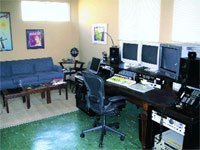 A room featuring a blue sofa, a coffee table, and a desk equipped with multiple computer monitors and audio gear.