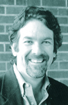 A smiling man with wavy hair and a beard wearing a collared shirt and jacket.