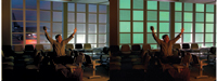 A man sits in a dark waiting room with his arms raised in celebration against a large window.