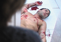 A shirtless man lies on white tiles with blood on his chest, arms, and hands.