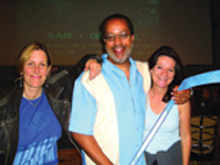 A man in a light blue shirt stands between two women, all smiling.