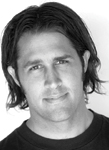 Black and white headshot of a man with dark, shoulder-length hair looking toward the camera.