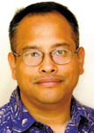 A man with short dark hair and glasses wearing a blue patterned button-down shirt.
