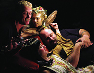 Four performers in elaborate costumes posing closely against a dark background.