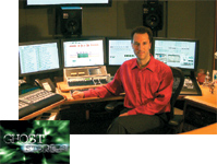 A man in a red shirt sits at a workstation with four computer monitors and audio equipment.