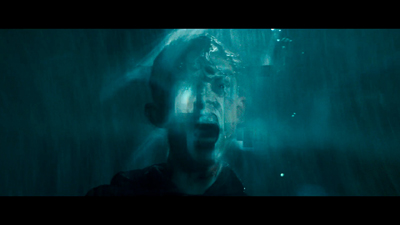 A man's face is submerged in dark blue water with bubbles and light streaks around him.