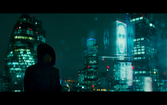 A hooded person in silhouette overlooks a glowing, futuristic city with a large digital face on a skyscraper.