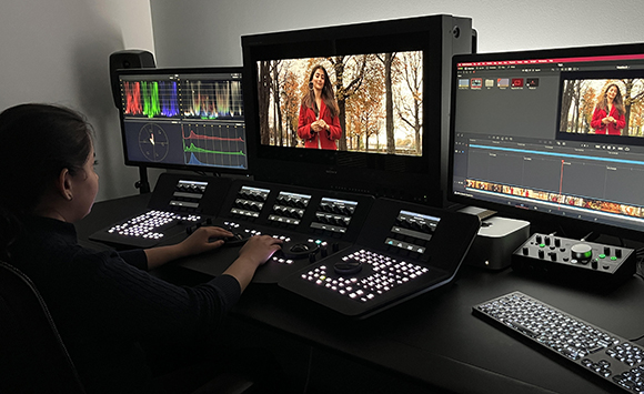 A person uses specialized control panels and multiple monitors to edit video in a dark studio.