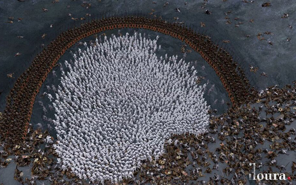An aerial view of a massive white army surrounded by a ring of dark-armored soldiers on a grey battlefield.