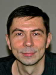 A close-up portrait of a man with short dark hair and a slight smile against a neutral background.