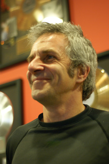 A man with graying hair smiling and looking upward against a red wall with framed awards.