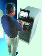 A man in a blue shirt and khaki pants operates a large, upright computer workstation.