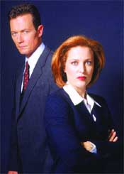 A man in a suit and a woman with red hair posing against a dark blue background.