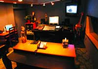 A recording studio with a mixing console, computer monitors, and a double bass in a dimly lit room.