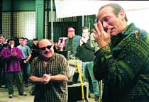 A man in a patterned green shirt covers his face while others clap in the background on a film set.