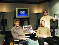 Two men sit in a studio with a large screen displaying the word DVD behind them.