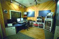 A recording studio featuring a mixing desk, computer monitors, and various audio equipment racks.