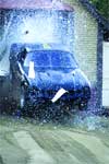 A blue car partially obscured by a large spray of water or white particles.