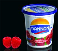 A white tub of Dannon raspberry yogurt sits next to two fresh red raspberries on a black background.
