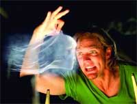 A person in a green shirt gestures toward a swirling white mist against a dark background.