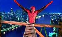 A superhero in a red and blue suit crouches on a bridge with arms outstretched over a city skyline at night.