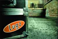 A black equipment case featuring an orange and white Lugz logo sits on a concrete floor.