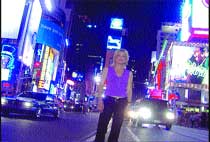 A woman in a purple top and dark pants stands on a city street surrounded by bright neon signs and cars.