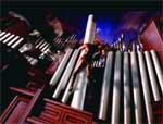 A person climbs between tall, silver organ pipes in a dimly lit room.