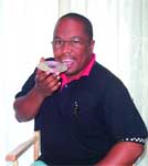 A man in a black polo shirt holds a compact disc up near his mouth and smiles.